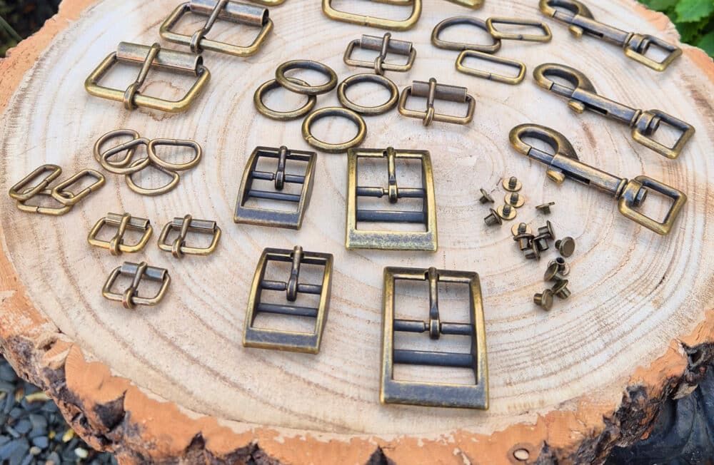 Antique brass hardware collection for dog collars displayed on wood, including buckles, rings, and fasteners.