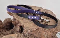 The Midnight Amethyst Two Colour Lead, featuring black and purple colours with sturdy metal fittings, is coiled and displayed on textured brown wood against a plain light background.