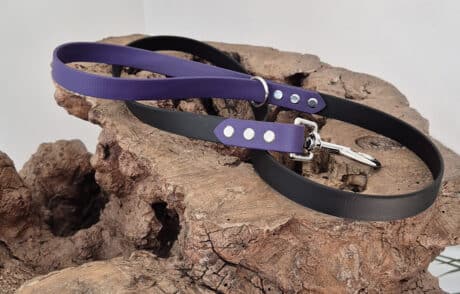 The Midnight Amethyst Two Colour Lead, featuring black and purple colours with sturdy metal fittings, is coiled and displayed on textured brown wood against a plain light background.