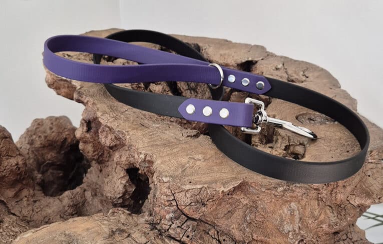 The Midnight Amethyst Two Colour Lead, featuring black and purple colours with sturdy metal fittings, is coiled and displayed on textured brown wood against a plain light background.