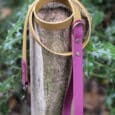 A tan and magenta dog lead is coiled and draped over a wooden post, with green foliage and blurred plants in the background.