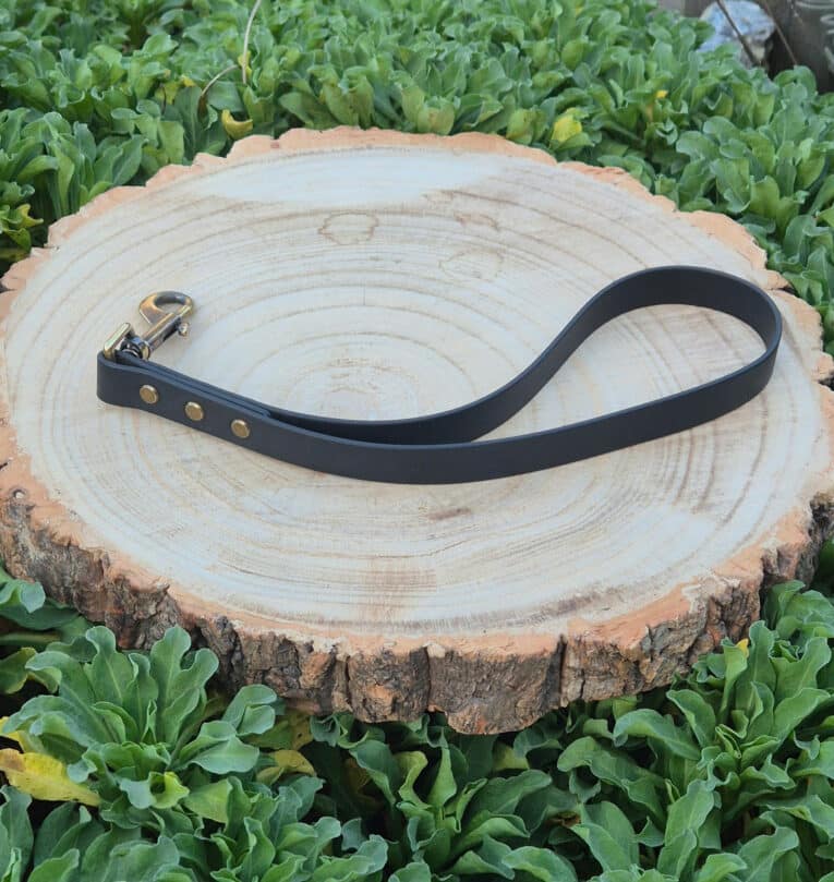 A Custom Single Colour Traffic Handle with a metal clasp lies coiled on a round tree stump, surrounded by green leafy plants.