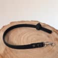 The Super-grip Biothane Training Tab / Obedience Lead 51cm, a short black textured dog lead with a metal clasp and customisable traffic handle, is coiled on a round light wooden surface against a plain white background.