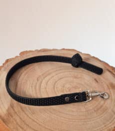 The Super-grip Biothane Training Tab / Obedience Lead 51cm, a short black textured dog lead with a metal clasp and customisable traffic handle, is coiled on a round light wooden surface against a plain white background.