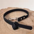 A Super-grip Biothane Training Tab / Obedience Lead 51cm with a black textured finish and silver metal clasp is neatly coiled on a round, light-coloured wooden surface.