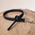 A black textured Super-grip Biothane Training Tab / Obedience Lead 51cm with a metal clasp is coiled neatly on a light wooden surface with visible tree rings.