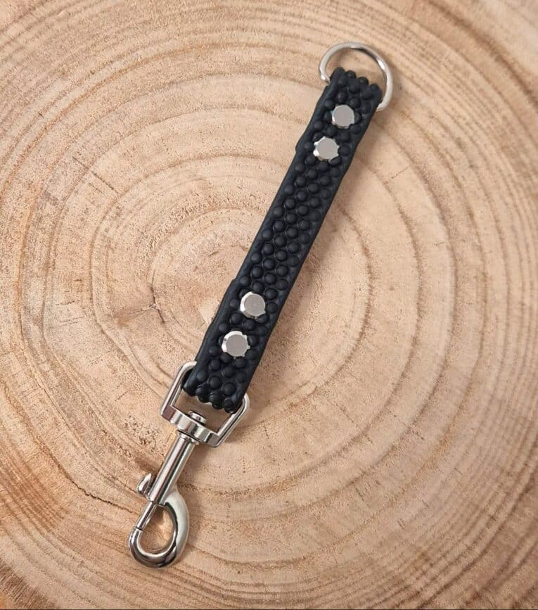 The Super-grip Biothane Training Tab/Obedience Lead - 51cm/20in (Copy), a black textured lead with silver studs and metal fittings, is displayed on a round wooden surface with visible tree rings.
