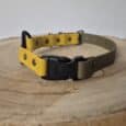 The Quick-Snap Bungee Collar, featuring yellow and olive green colours with a black quick-snap buckle, rests on a round wooden surface displaying visible tree rings.