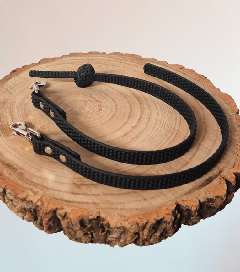 A Super-grip Biothane Training Tab / Obedience Lead 51cm with metal clasps is coiled on a round wooden slice with visible tree rings, set against a light background.