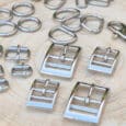 Various shiny silver metal hardware pieces, including best dog lead fittings such as buckles, D-rings, clasps, and screws, are arranged neatly on a light-coloured wooden surface—ideal for crafting or assembling quality dog collars.