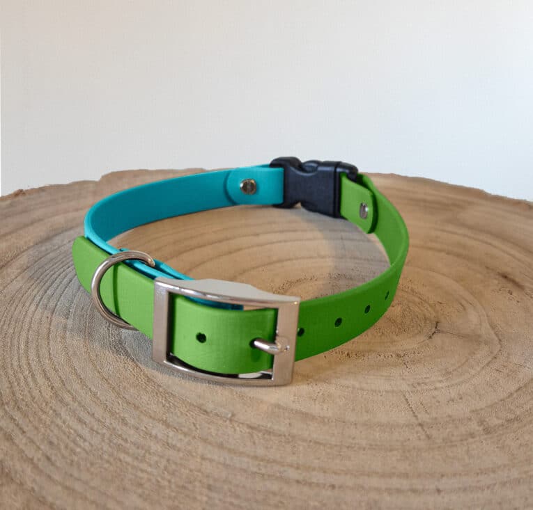 A Custom Quick-Snap Bungee Collar (Copy) in green and blue, featuring a silver buckle and D-ring, displayed on a wooden surface with visible tree rings.