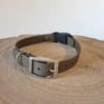 The Custom Quick-Snap Bungee Collar (Copy) in olive green, featuring a silver buckle and metal D-ring, is shown coiled on a round, textured wooden surface with visible tree rings.