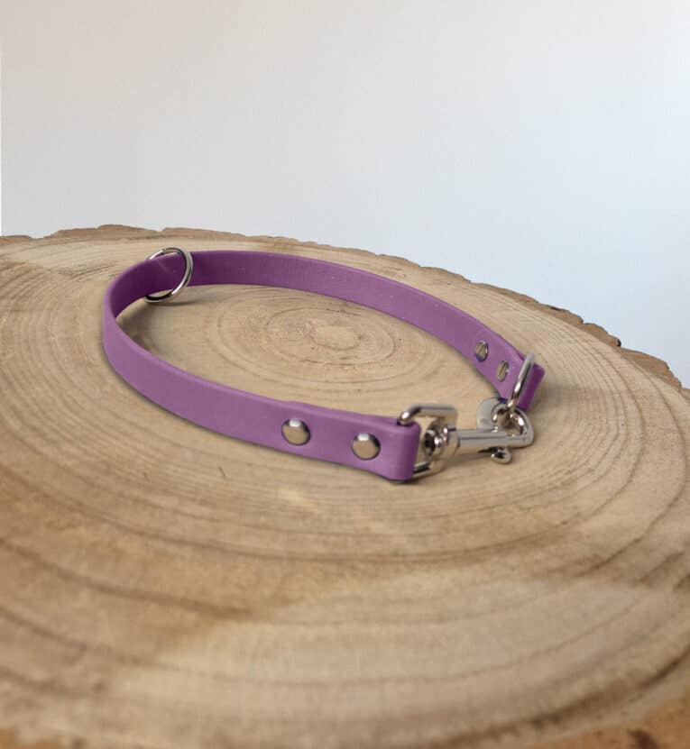 A lavender-coloured dog collar with metal studs and a clasp, displayed on a round wooden surface with visible rings.