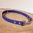A purple dog collar with metal rivets, a D-ring, and a clasp is displayed on a round, light-coloured wooden surface.