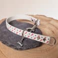 The Custom Snap Tag - Slip Collar features a white design with red horses and black horseshoes, metal fittings, and a small silver bone charm, shown on dark stone set on wood.