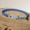 A two-tone dog collar with dark blue and light blue sections, bronze metal rings, and rivets rests on a cut tree stump with visible growth rings.