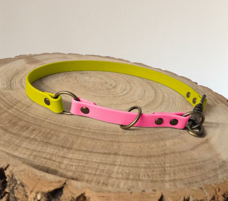 A dog collar with a neon yellow band and a pink section, made of synthetic material with metal fittings, is displayed on a round wooden surface.
