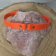 The Centre O-Ring Collar / Gundog Collar, featuring metal fittings and an orange design, is shown draped over a large pink crystal on a round wooden surface.