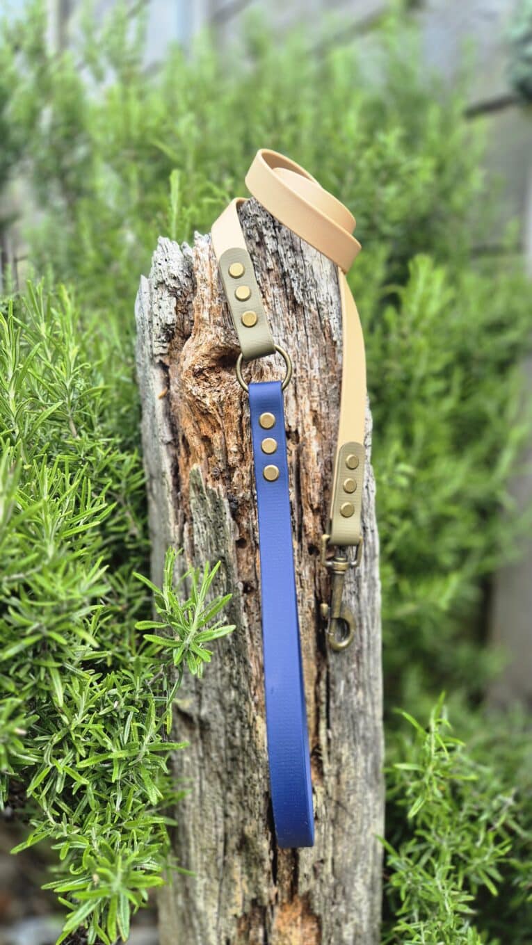 Aubreys x Lutchfords collaboration BioThane lead in navy blue and beige with antique brass hardware, displayed on weathered wood.