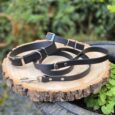Three black BioThane 1.2m leads with customisable hardware options displayed on a wood slice in a garden setting.