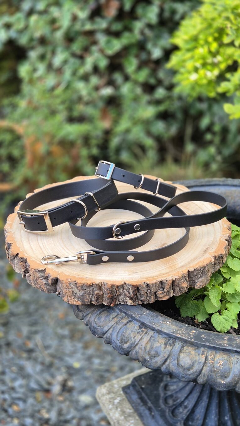 Three black BioThane 1.2m leads with customisable hardware options displayed on a wood slice in a garden setting.