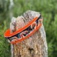 Printed double layer hound collar in orange and black dragon design, displayed on wooden post with garden background.