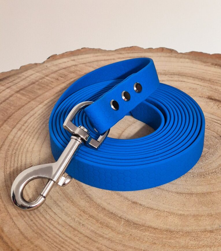 Bright blue waterproof longline coiled on natural wood, featuring silver hardware and textured BioThane handle with three eyelets.
