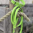 Bright lime green BioThane 1.2m lead with stainless steel hardware, draped over weathered wooden post beside rope.