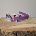 Multicoloured printed tapered BioThane dog collar with purple straps and metal hardware on wooden surface.