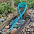 Bright blue BioThane hands-free lead wrapped around wooden post in garden setting, demonstrating versatile multi-way double-ended configuration.