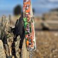 Adjustable martingale half-check collar in printed BioThane, displayed on weathered wood by the shore.