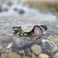 Colourful printed extra wide waterproof BioThane collar positioned on beach stones with coastal backdrop