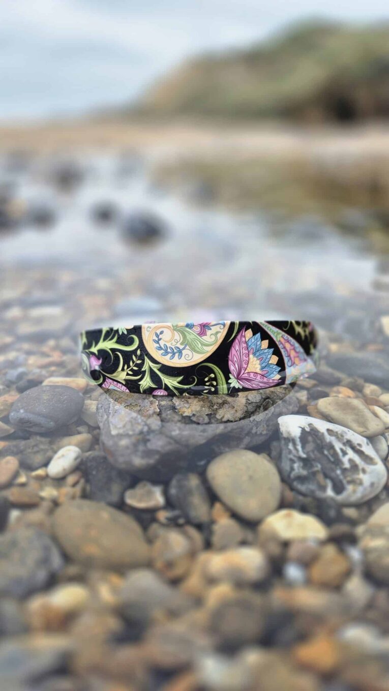 Colourful printed extra wide waterproof BioThane collar positioned on beach stones with coastal backdrop
