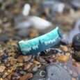 Forest print tapered hound collar in turquoise and teal displayed on coastal pebbles and rocks.