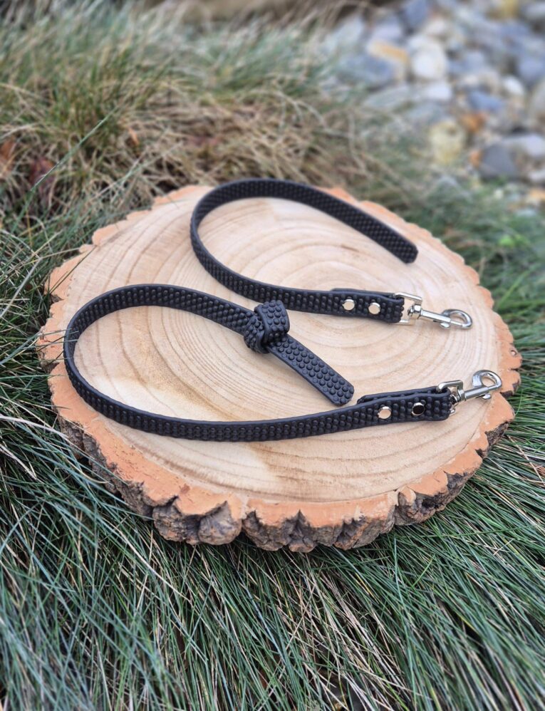 Two black Super-Grip Waterproof Training Tab Obedience Leads displayed on a wood slice, featuring textured grip handles and nickel hardware.