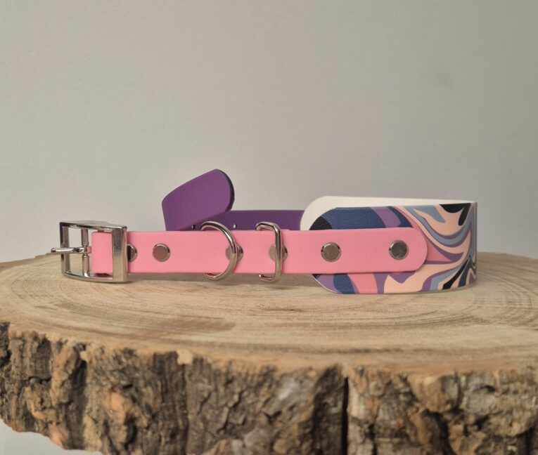 Pink waterproof BioThane hound collar with patterned design, metal D-rings, and buckle hardware displayed on wooden surface.