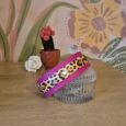 Leopard print double layer hound collar in pink and cream, displayed on a glass pot with floral backdrop.