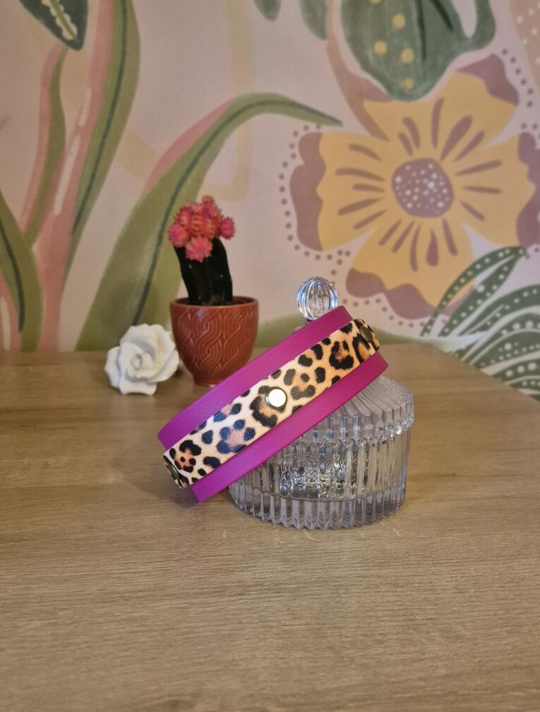 Leopard print double layer hound collar in pink and cream, displayed on a glass pot with floral backdrop.