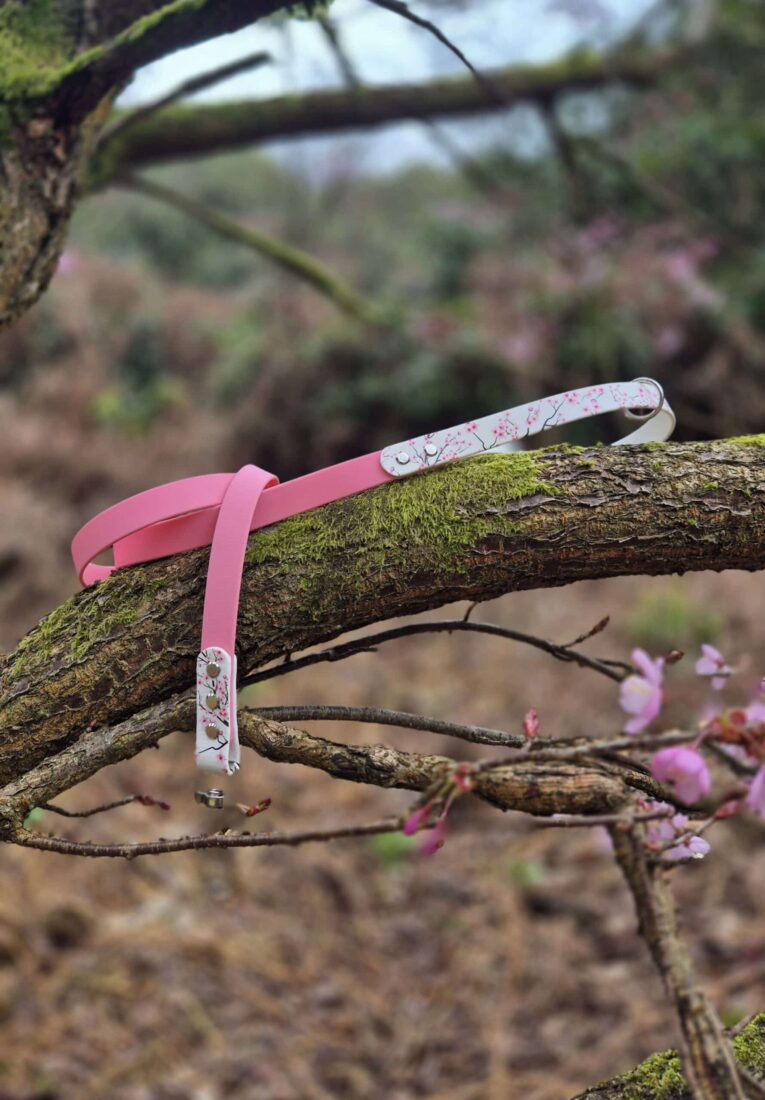 Pink BioThane dog lead with floral printed handle, draped over moss-covered branch with blooming flowers.