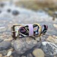 Waterproof wide floral printed BioThane collar with lavender strap and antique brass hardware, positioned on coastal rocks.