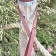 Custom Biothane lead in dusty rose with antique brass hardware, displayed on wooden post amongst garden foliage.