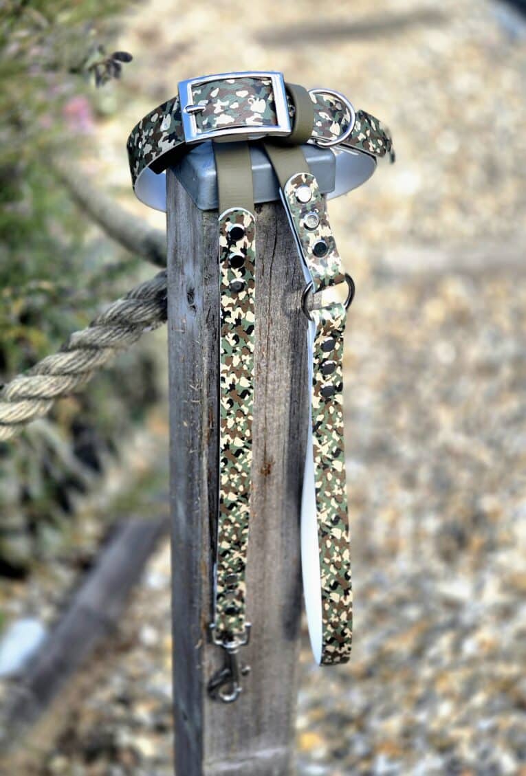 Camouflage printed BioThane lead with stainless steel hardware and D-ring, displayed on weathered wood post.