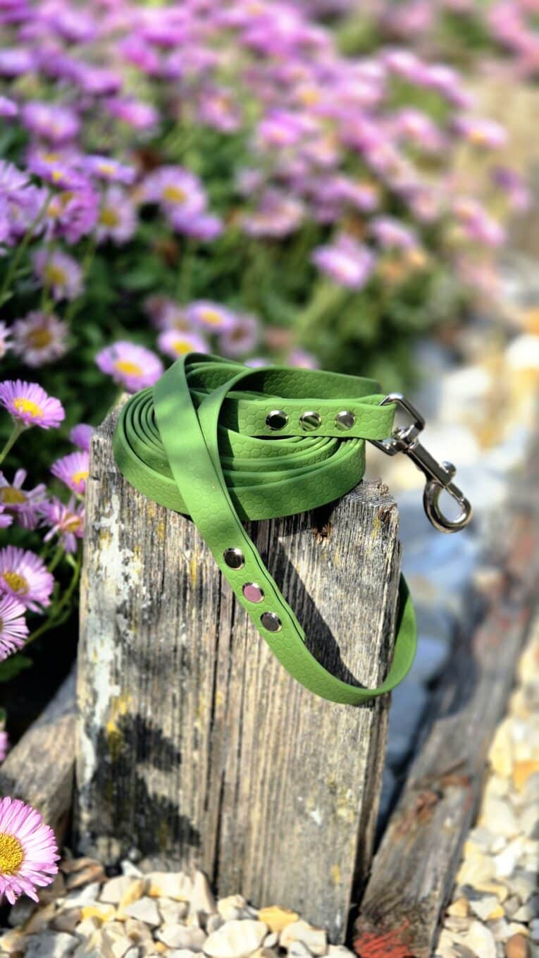 Bright green waterproof longline with metal hardware coiled on weathered wood, surrounded by purple flowers.