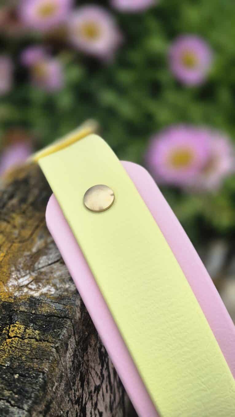 Custom double layer hound collar in pale yellow and pink with stainless steel hardware, displayed on weathered wood with flowers.